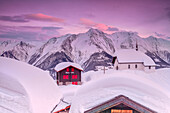 Pink sky at sunset frames the snowy mountain huts and church, Bettmeralp, district of Raron, canton of Valais, Switzerland, Europe