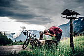 Junger Mountainbiker erfrischt sich an einer Hütte an einem Brunnen im Brandnertal, Vorarlberg, Österreich, Berge, Hütte