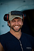Boat engineer smiles at the camera with ear protection over head.