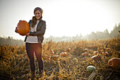 A young woman holds a medium sized pumkin while at the pumpkin patch.