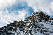 Snow covered mountain peak with clouds rolling over top and blue sky, Alberta, Canada