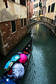 A gondola traveling through a canal on a rainy day with the passengers holding umbrellas, Venice, Italy