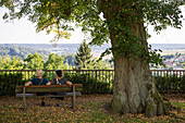 Ein Paar sitzt auf einer Bank unter einer alten Linde in Frankenberg (Eder) auf dem Burgberg, Nordhessen, Hessen, Deutschland, Europa