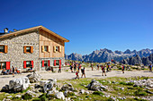 Mehrere Personen wandern an der Lavaredo-Hütte vorbei, Dolomiten im Hintergrund, Lavaredo-Hütte, Sextener Dolomiten, Dolomiten, UNESCO Weltnaturerbe Dolomiten, Südtirol, Italien