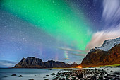 Aurora borealis, Polarlicht über Strand und beleuchteter Ortschaft, Lofoten, Norland, Norwegen