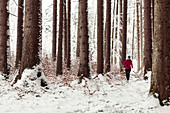Junge Frau joggt durch verschneiten Wald in Berg am Starnberger See, Bayern, Deutschland.