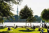 Locals and tourists taking a break at lake Aussenalster with a view to the television tower, Hamburg, Germany
