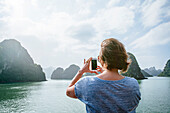 Caucasian woman photographing rock formations in Ha Long Bay, Vietnam