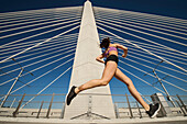 Low angle view of Caucasian woman jogging on urban bridge