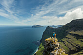 Mann steht auf der Spitze eines Felsen in den Bergen, Färöer Inseln