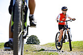 Kinder fahren mit ihren Fahrrädern neben einer Wiese, Füssen, Bayern, Deutschland