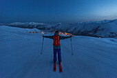 Junger Skifahrer fährt während der Abendämmerung einen Berg zu einem Dorf herunter/ Gudauri, Mzcheta-Mtianeti, Georgien