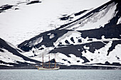 Sailing bark Europa and snow-covered volcanic landscape Telefon Bay, Deception Island, South Shetland Islands, Antarctica