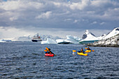 Passagiere von Expeditions Kreuzfahrtschiff MV Sea Spirit (Poseidon Expeditions) paddeln im Seekajak entlang Eisschollen und Eisbergen, Cuverville Island, Grahamland, Antarktische Halbinsel, Antarktis