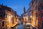 Beleuchtete Häuser am Rio di San Barnaba mit Turm der Kirche Santa Maria dei Carmini und Booten im Blau der Dämmerung, Dorsoduro, Venedig, Venezien, Italien