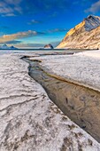 The golden sunrise reflected in a clear stream of the sea where the snow has melted. Haukland Lofoten Islands Norway Europe.