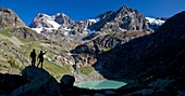 Hikers looking at the glaciers and the peaks of the Bernina Group not far from the Lake of Alp Gera (Lago dell'Alpe Gera), Valmalenco, Valtellina, Lombardy Italy Europe.