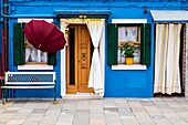 Burano, Venice, Veneto, North East Italy, Europe. Umbrella in front of colored facade in Burano.