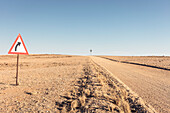 Windrad, und Warnschild vor der Kurve einer der unfallträchtigen Sandpisten, Erongo, Namibia, Afrika