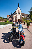 Motorcycle riders look at map outside Kloster Bronnbach abbey along Romantische Strasse romantic road through Unteres Taubertal, Bronnbach, near Wertheim, Spessart-Mainland, Franconia, Baden-Wuerttemberg, Germany