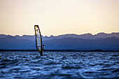 Junger Mann windsurft bei Sonnenuntergang, Ammersee, Bayern, Deutschland