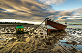 'A wooden boat tied to the shore sitting on wet sand at the water's edge at sunset; Whitburn, Tyne and Wear, England'