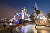 The Girl With A Dolphin Fountain frames Tower Bridge reflected in the River Thames at night, London, England, United Kingdom, Europe