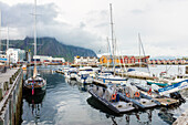 Clouds on rocky peaks frame the boats in the harbor of the fishing village of Svolvaer, Vagan, Lofoten Islands, Norway, Scandinavia, Europe