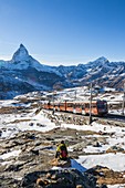 Hiker admires Matterhorn while white train of Gornergrat rides in the background, Zermatt, Canton of Valais, Switzerland Europe