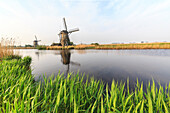 Green grass frames the windmills reflected in the canal Kinderdijk Rotterdam South Holland Netherlands Europe