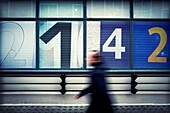 Un hombre andando en movimiento irreconocile, al fondo una fachada con numeros 2-1-4-2. London, UK, Europa.