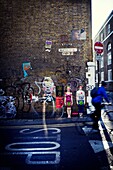 Un ciclista irreconocible circulando por una calle y en la pared de fondo pintada con graffitis. Buxton St. East End, London, UK, Europa.