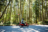 Person riding scooter on road near forest