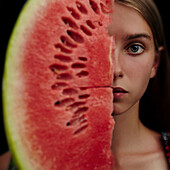 Caucasian girl holding slice of watermelon over half of face