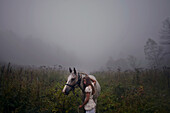Caucasian girl petting horse in foggy field