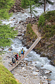 Hikers cross the wooden bridge on a creek in the woods Minor Valley High Valtellina Livigno Lombardy Italy Europe