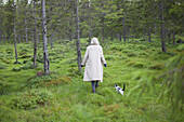 Rear view of woman wearing long coat while walking with cat on grassy field