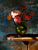 Green terracotta vase on a bench with zinnia flowers
