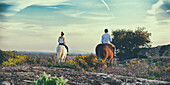 Spain, Los Santos, Man and woman horse riding seen from behind