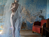 Front view of a female nude moving covered with a veil next to a red armchair