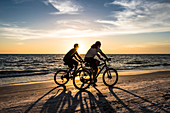 Zwei Radfahrer am Strand zum Sonnenuntergang am Golf von Mexiko, Fort Myers Beach, Florida, USA