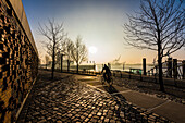 Ein Radfahrer nach Sonnenaufgang am Dalmannkai in der Hafencity mit Blick auf die Elbe, Hamburg, Deutschland