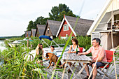 Familie enjoying evening on terrace at their boat house, thatched roof, dog, boathouses at Granzower Möschen, holiday, summer, Mecklenburg lakes, Mecklenburg lake district, Granzow, Mecklenburg-West Pomerania, Germany, Europe