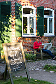 Man on bench, traditional house, restaurant, Lake hotel Neuklostersee, holiday, Mecklenburg lakes, Mecklenburg lake district, Neukloster, Mecklenburg-West Pomerania, Germany, Europe