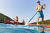 Stand up paddling on lake, boy with paddle, red SUP, girls in red boat, canoe, kayak, water sports, crystal clear green water, lake Schmaler Luzin, holiday, summer, swimming, MR, Feldberg, Mecklenburg lakes, Mecklenburg lake district, Mecklenburg-West Pom