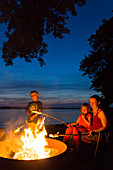 family at campfire in twilight, suset, baot, beach at lake Plauer See, camping ground, willow, sunset, beach chair, swimming, summer, Mecklenburg lakes, Mecklenburg lake district, Zislow, Mecklenburg-West Pomerania, Germany, Europe