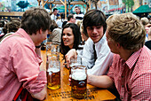Young people in traditional cloth with beer mugs to toast at Oktoberfest, Munich, Bavaria, Germany