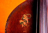 'Detail of an old-time stand up bass from the 1920's is adorned with a decal featuring a blonde pin-up girl'' and serpent.'''