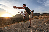 A young man and woman perform Yoga in the desert at sunset.