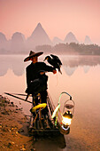 Chinese fisherman fishes with cormorant birds on a bamboo raft in Li Jang River, Yangshuo, Guilin, Guangxi region, China on December 25, 2006. Like their ancestors, this fisherman uses cormorants to fish at dusk and dawn, using lamps to help the birds cat